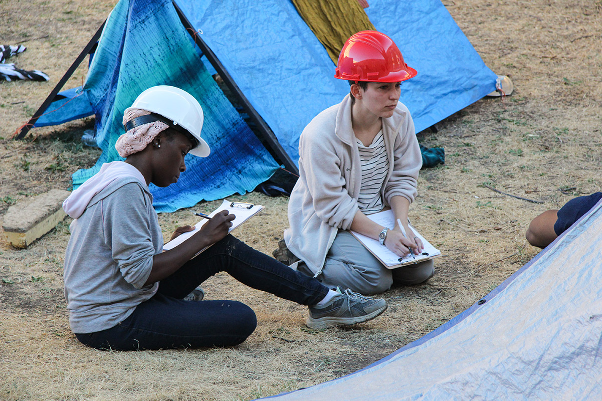 两个戴着安全帽的学生在灾难准备演习中做笔记