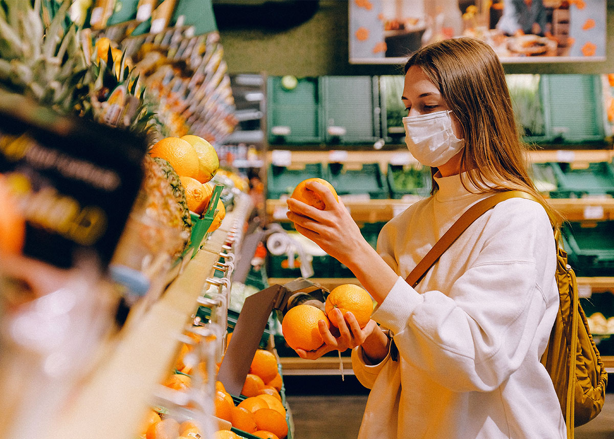 一个人戴着口罩在杂货店，拿着一个橘子在水果摊