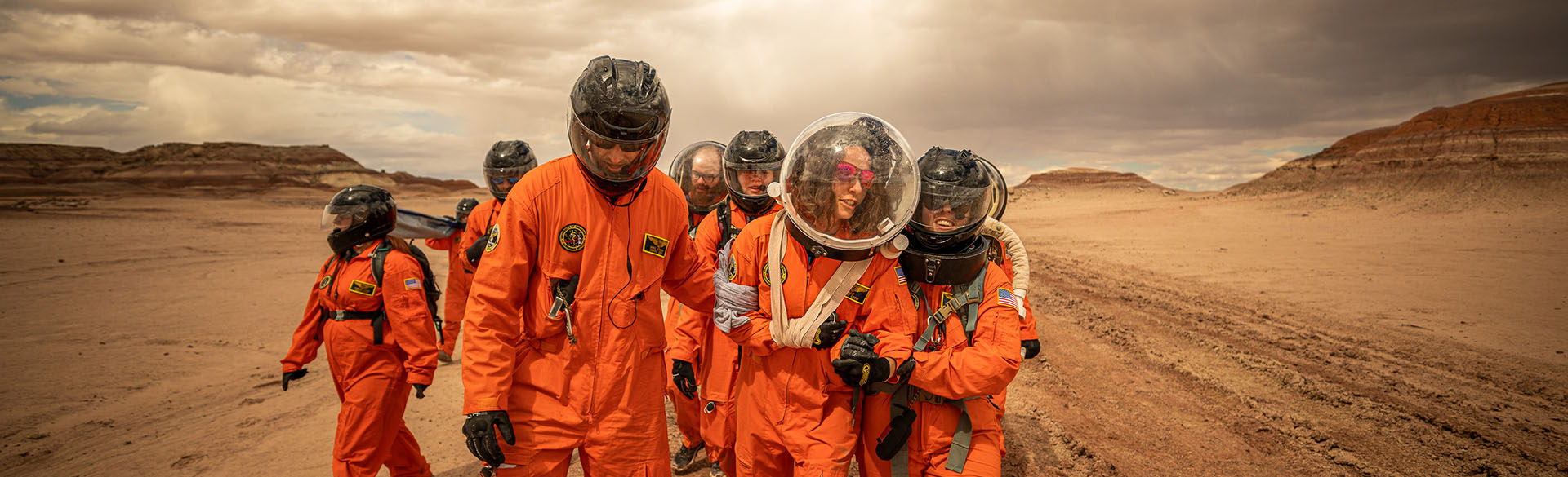 学生和老师们穿着橙色的太空服，戴着太空头盔，在沙漠中训练